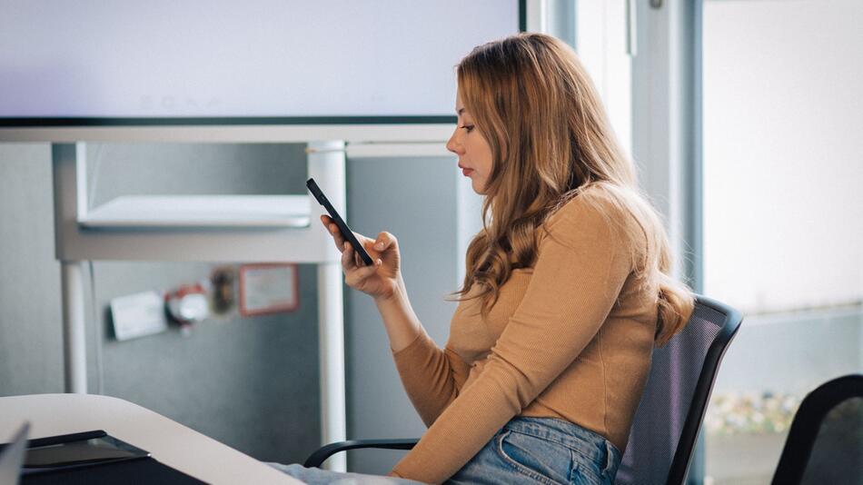 Eine Frau blickt auf ihr Smartphone in einem Konferenzraum