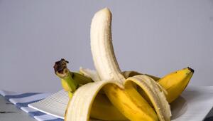 Eine teilweise geschälte Banane liegt auf mehreren ungeschälten Bananen, die auf einem weißen ...