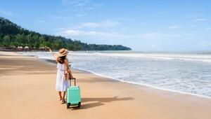 Eine Touristin steht mit ihrem Koffer am Sandstrand.