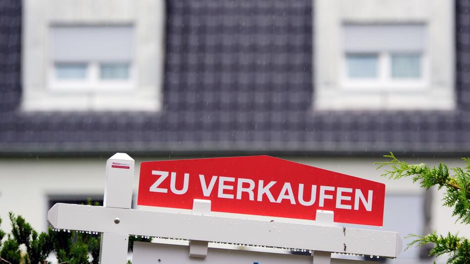 Ein Schild "Zu Verkaufen" steht vor einem Wohnhaus