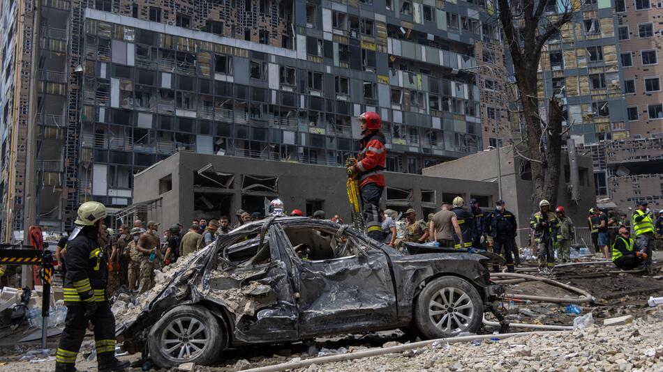 Ein Feuerwehrmann steht auf einem verbrannten Auto vor dem zerstörten Kinderkrankenhaus.