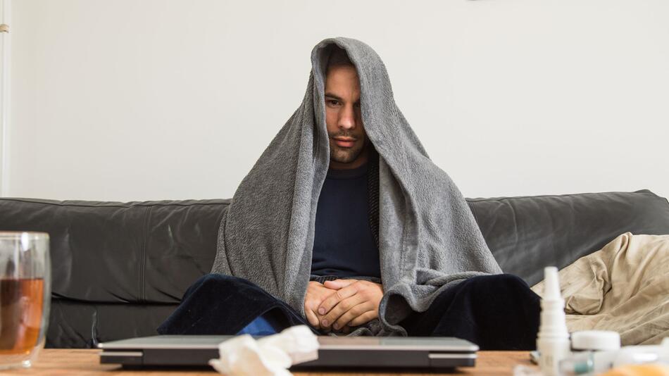 Ein Mann sitzt mit Erkältung auf der Couch