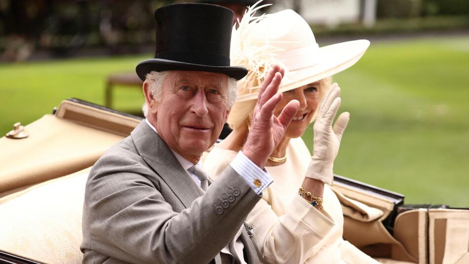 König Charles und Königin Camilla grüßen aus einer fahrenden Kutsche