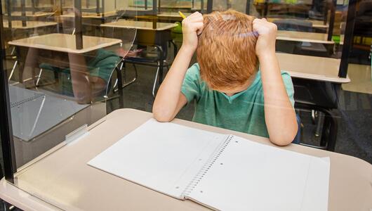 Ein Junge sitzt mit gesenktem Kopf allein an seinem Schultisch.