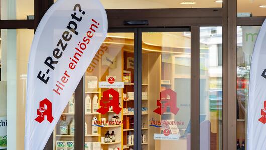 Eingang einer Apotheke mit Fahne zum E-Rezept