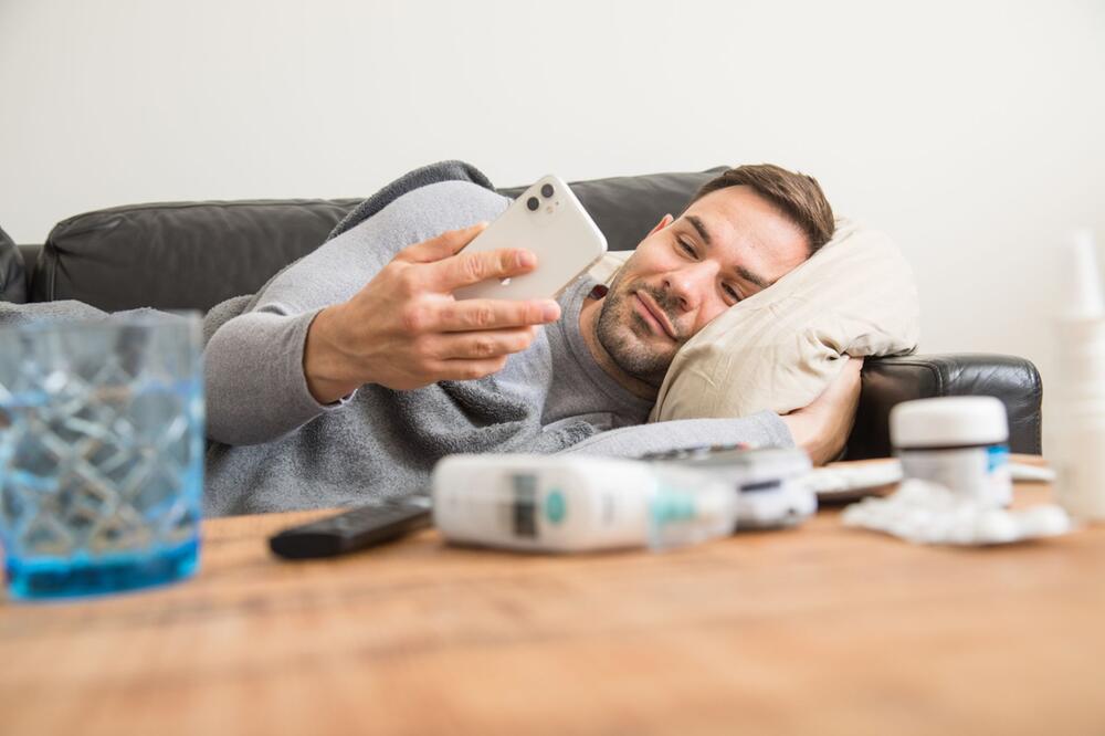 Ein Mann liegt auf einem Sofa und schaut auf ein Smartphone