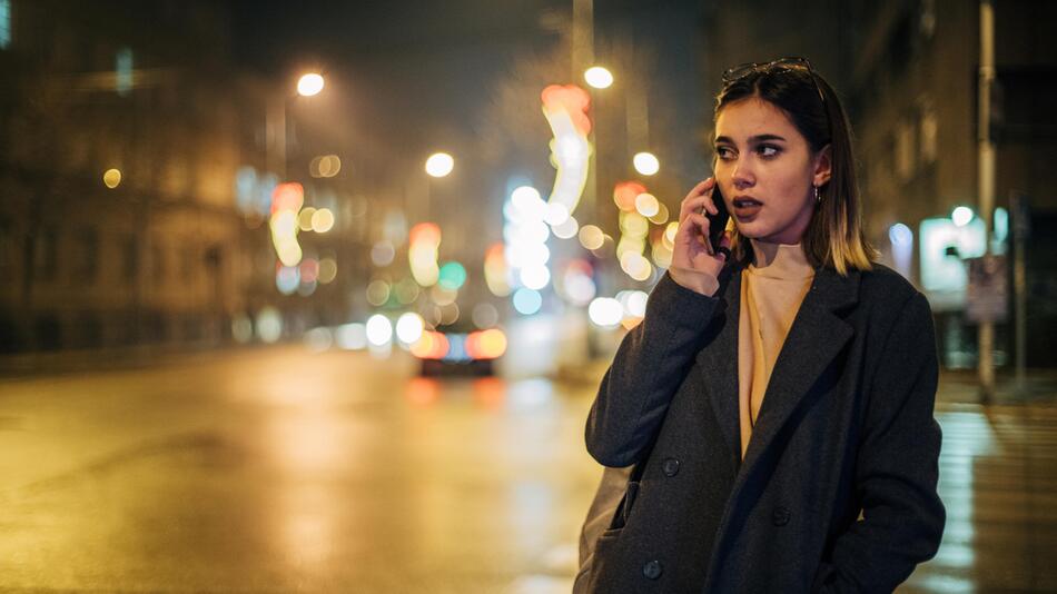 junge Frau telefoniert auf der dunklen Straße