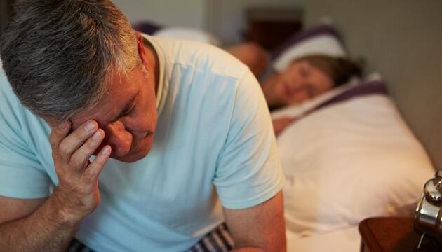 Mann, der an Bettkante sitzt und ernst schaut. 