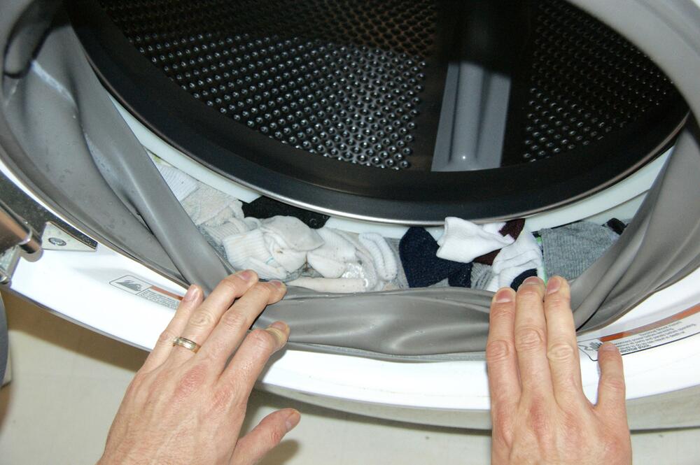 Hände ziehen am Gummiring der Waschmaschine. Dort sind Socken drin.
