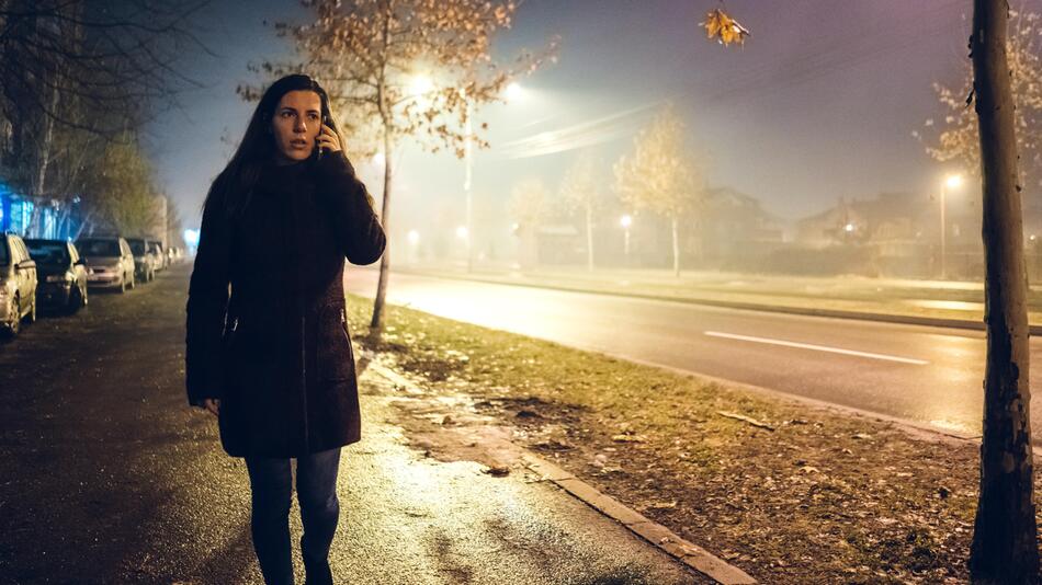 junge Frau telefoniert auf der dunklen Straße