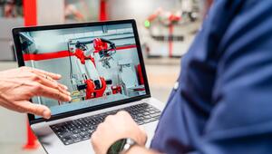 Beschäftigte betrachten auf einem Laptop die Steuerung eines Industrieroboters.