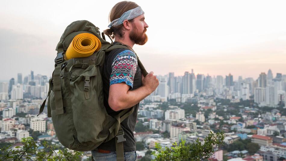 Mann mit Rucksack steht vor der Skyline einer Stadt