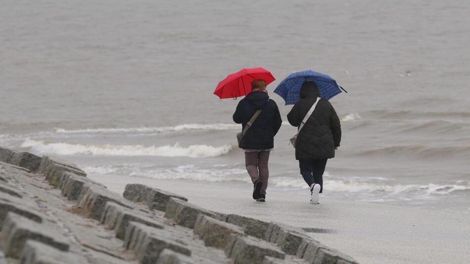 Zwei Menschen laufen mit Regenschirm einen Strand entlang.