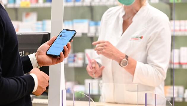 Mann zeigt auf einem Smartphone ein E-Rezept in einer Apotheke