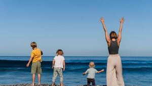 Eine Frau streckt die Hände jubelnd in die Höhe. Neben ihr an einem Steinstrand stehen drei Kinder.