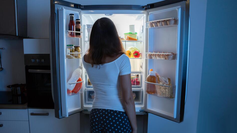 Frau steht nachts am offenen Kühlschrank