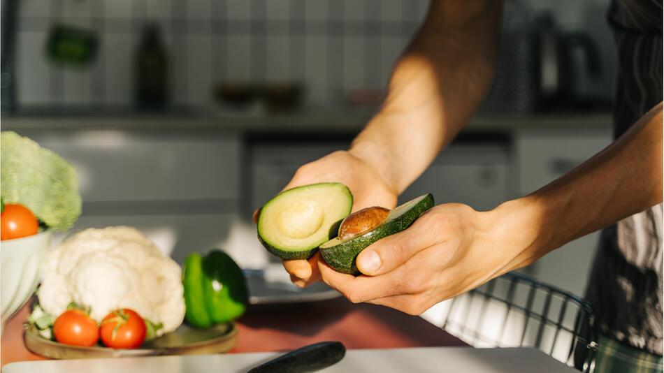 Zwei Hände halten eine aufgeschnittene Avocado.