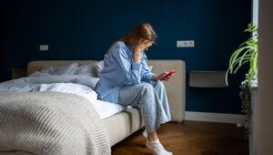 Eine traurige Frau sitzt mit ihrem Smartphone in der Hand auf dem Bett
