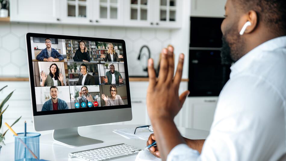 Mann winkt seinen Kollegen in einem Online-Meeting aus dem Homeoffice zu