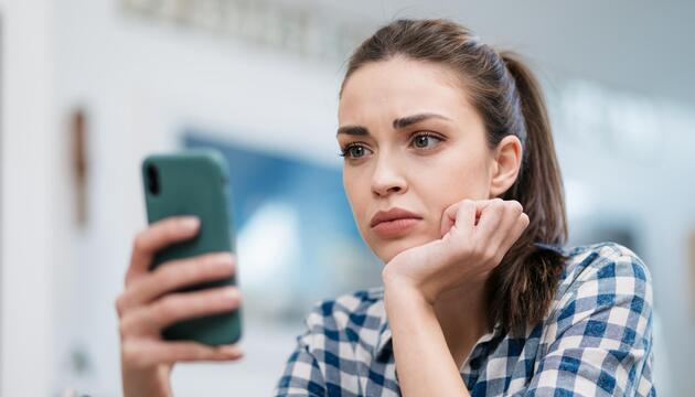 Junge Frau blickt skeptisch auf ihr Smartphone