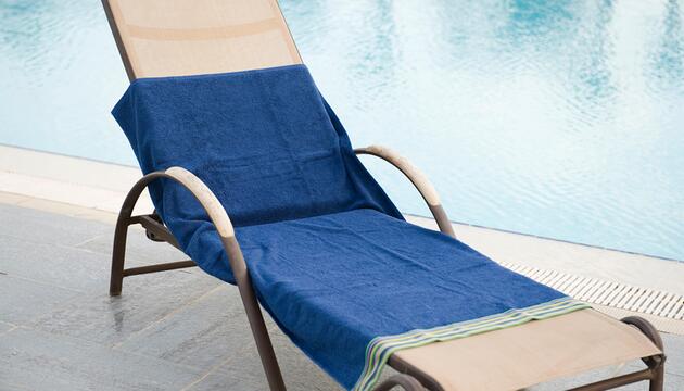 Eine lächelnde Frau legt am Pool ihr Handtuch auf eine Liege.