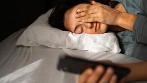 Junge Frau liegt müde im Bett und blickt auf ihr Smartphone