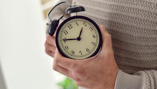 Person dreht an der Uhr, Zeitumstellung