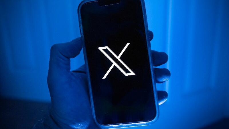 Eine Hand hält ein Handy mit Logo der Onlineplattform X.