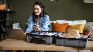 Frau sitzt mit Laptop und Smartphone vor ihrem Koffer.