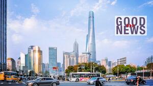 Straßenkreuzung in Shanghai mit Hochhäuser-Skyline im Hintergrund, rechts oben der Schriftzug ...