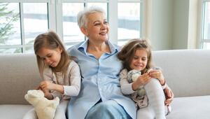 Eine Oma sitzt mit zwei Enkelinnen an ihrer Seite auf dem Sofa.