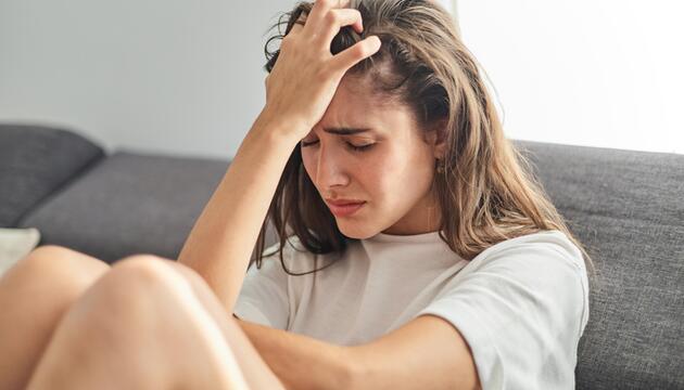Junge Frau sitzt auf dem Sofa, sie scheint verzweifelt