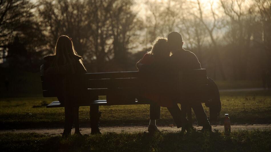 Drei Personen sitzen auf einer Parkbank