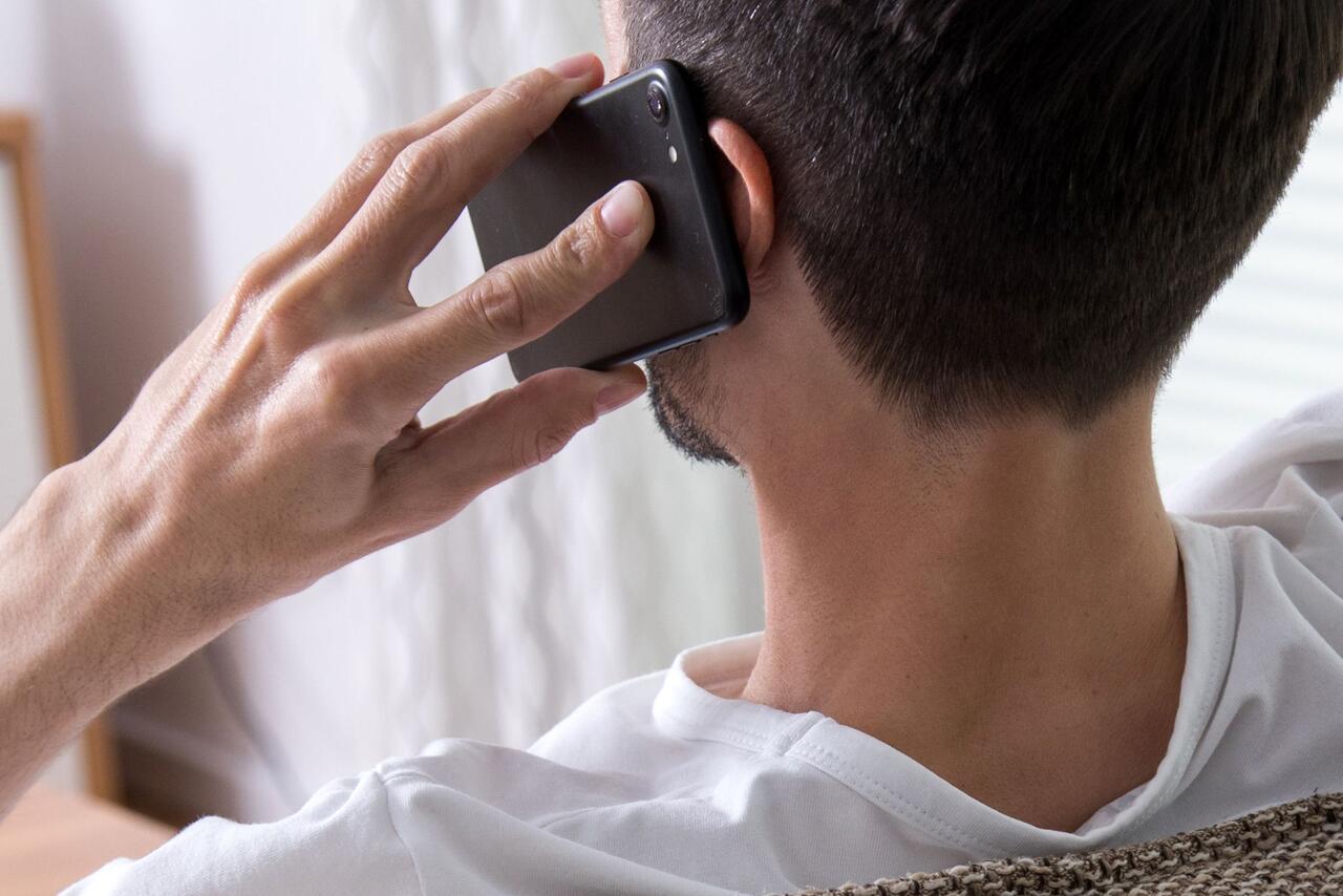 Bild zu Ein Mann sitzt telefonierend auf der Couch.