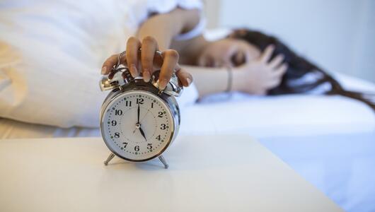 Frau liegt im Bett und schaltet morgens um 5 Uhr den Wecker aus.