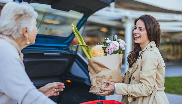 Frau hilft älterer Dame beim Einladen der Einkäufe 