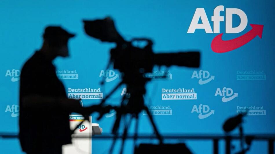 Ein Kameramann steht vor dem Logo der AfD.