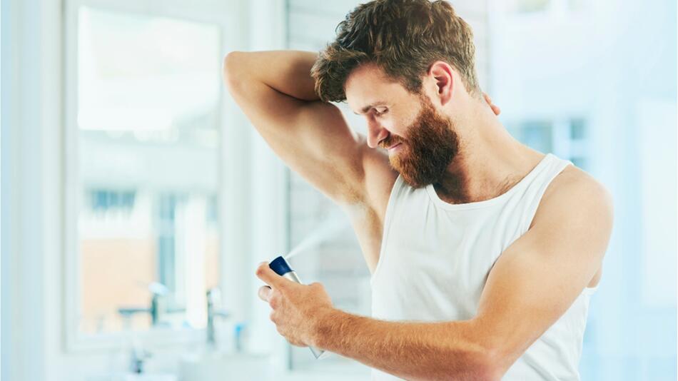 Mann sprüht Deodorant auf seine Achseln.