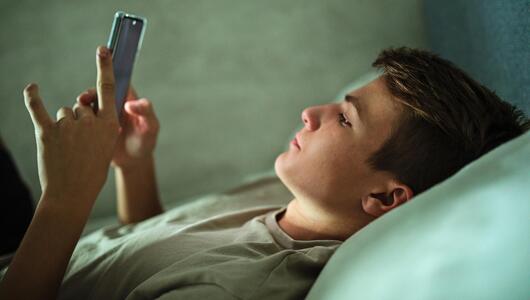 Ein Jugendlicher liegt einsam im Bett und starrt auf sein Smartphone