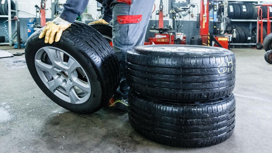Mitarbeiter einer Werkstatt rollt einen Sommerreifen zum Auto