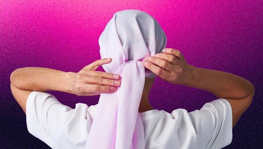 Frau, die sich ein Kopftuch bindet vor einem pink-lila Hintergrund. 
