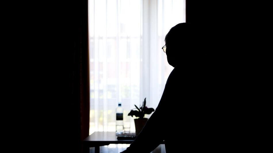 Ein Senior steht in einem Raum am Fenster