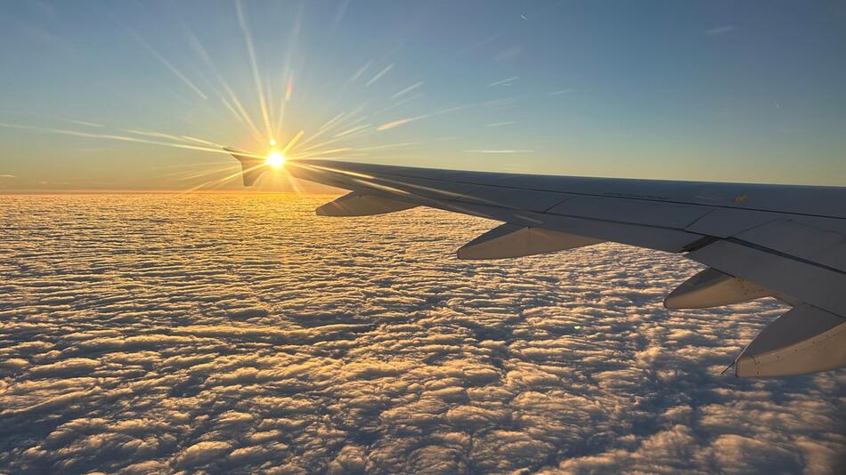 Die Sonne geht hinter dem Flügel eines Flugzeugs unter