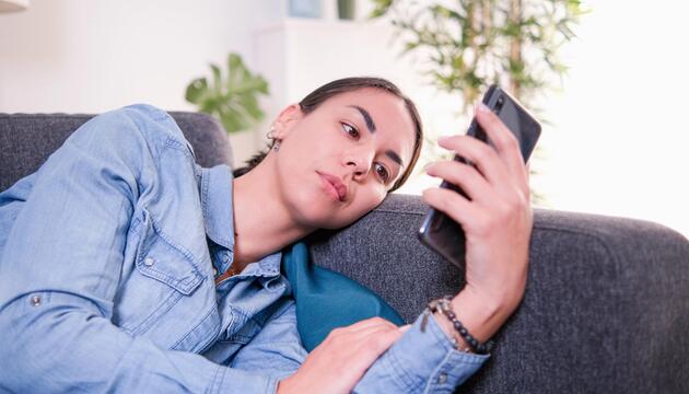 Eine Frau schaut enttäuscht auf ihr Handy.