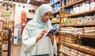 Muslimische Frau in einem Supermarktgang prüft via App, ob die Lebensmittel halal sind.