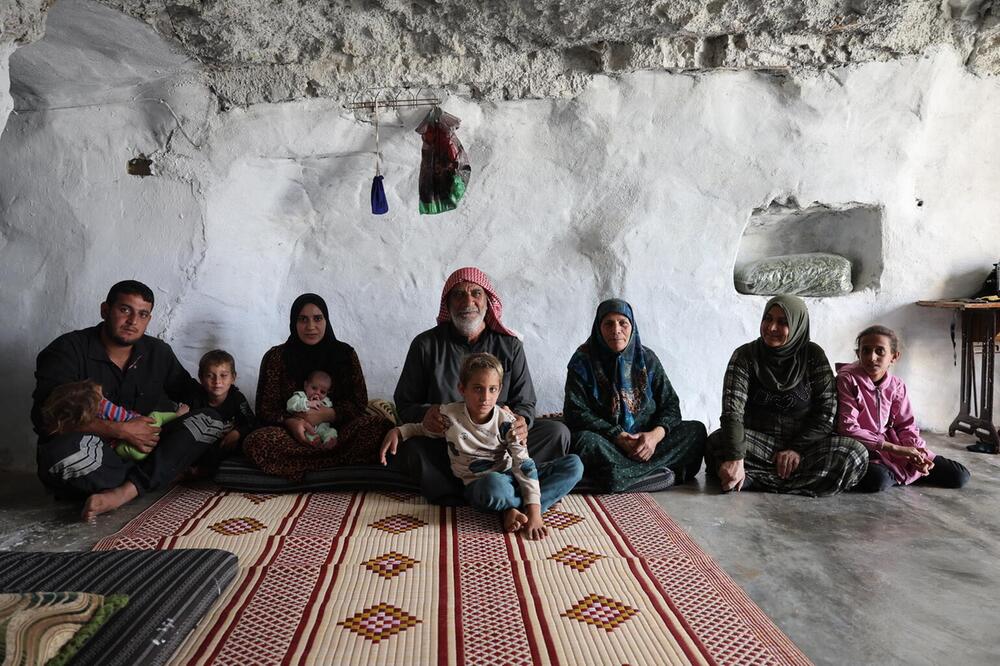 Fünf Erwachsene und mehrere Kinder sitzen vor einer weißen Wand in einer Höhle.
