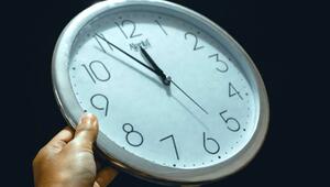 Hand hält eine runde Wanduhr mit weißem Zifferblatt und schwarzen Zahlen, die Uhrzeit zeigt 11 ...