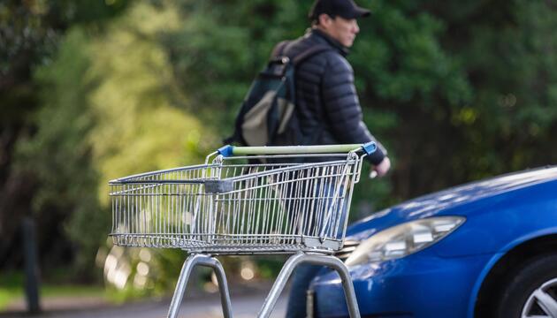 Mann geht weg zum Auto, im Vordergrund ein Einkaufswagen