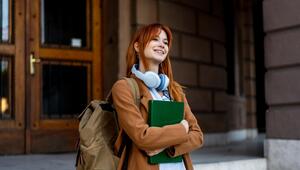 Frau steht mit Büchern vor Universität 
