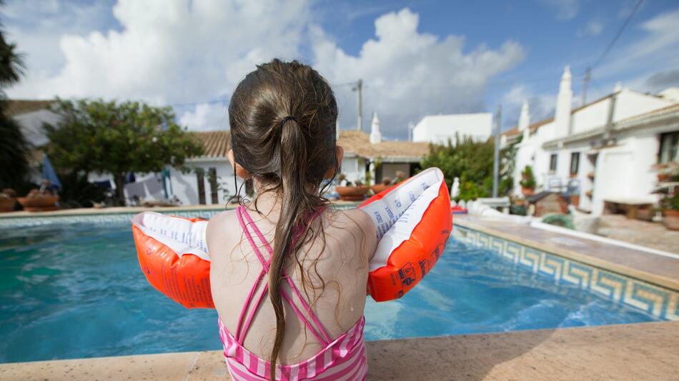 Kleines Mädchen sitzt mit Schwimmflügeln am Pool.